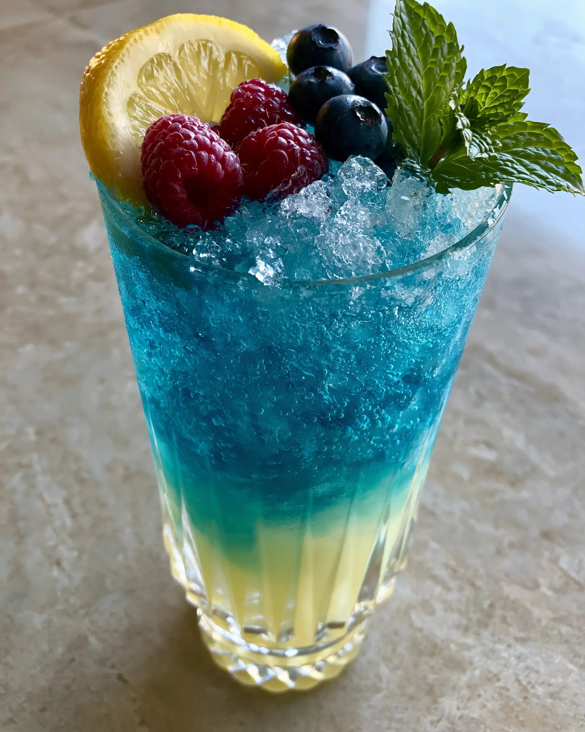 Close up of blue raspberry lemonade in a ribbed glass showing condensation and fresh berries. (blue raspberry lemonade)