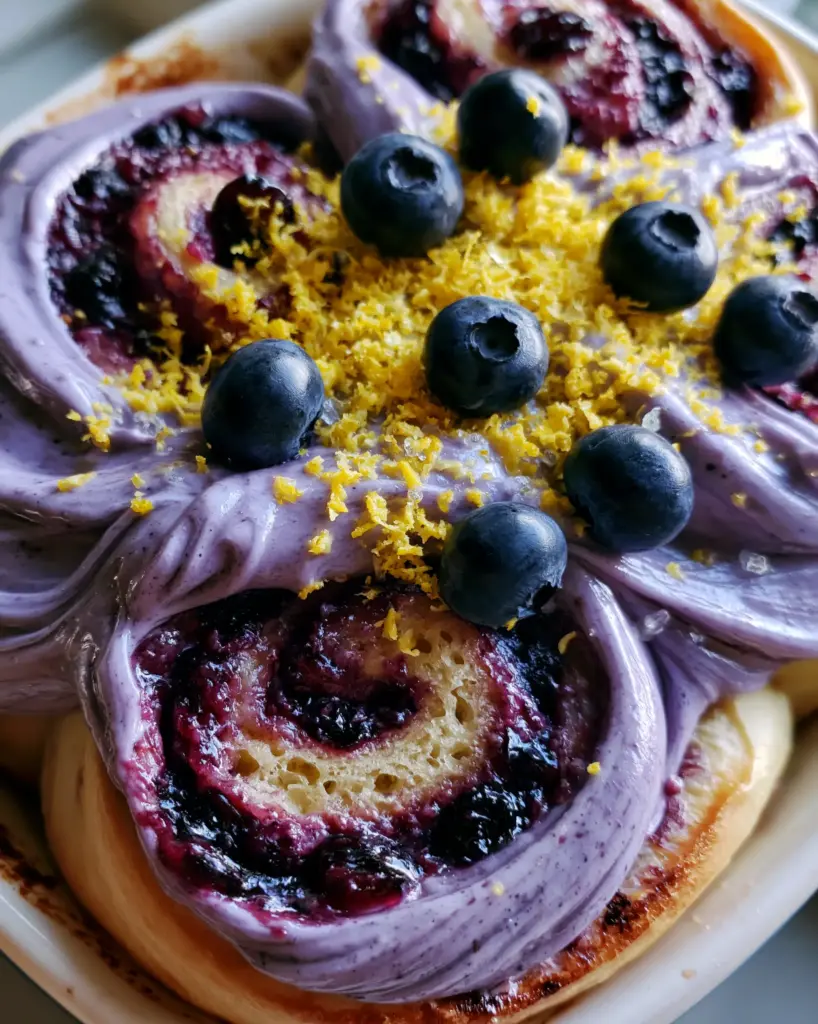 Pull-apart blueberry cinnamon rolls showing the toasted golden-brown crust and pale lavender swirls of icing.