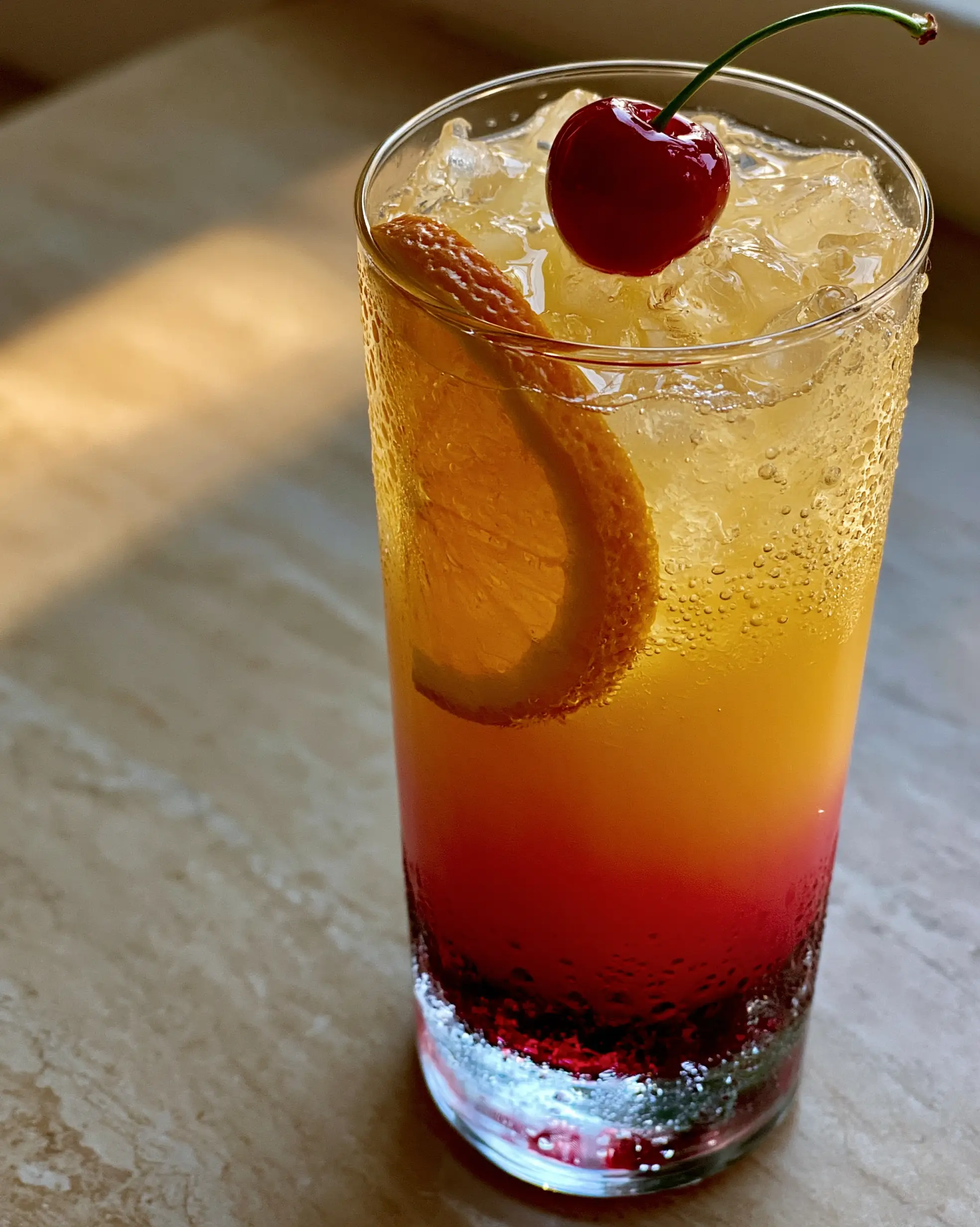 Close-up photograph showing the crimson, orange, and yellow layers of a Malibu Sunrise cocktail.