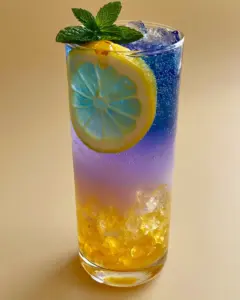 Close up of a layered Honey Lemon Butterfly Fizz mocktail showing sparkling water bubbles and a vivid blue tea top layer in natural daylight.