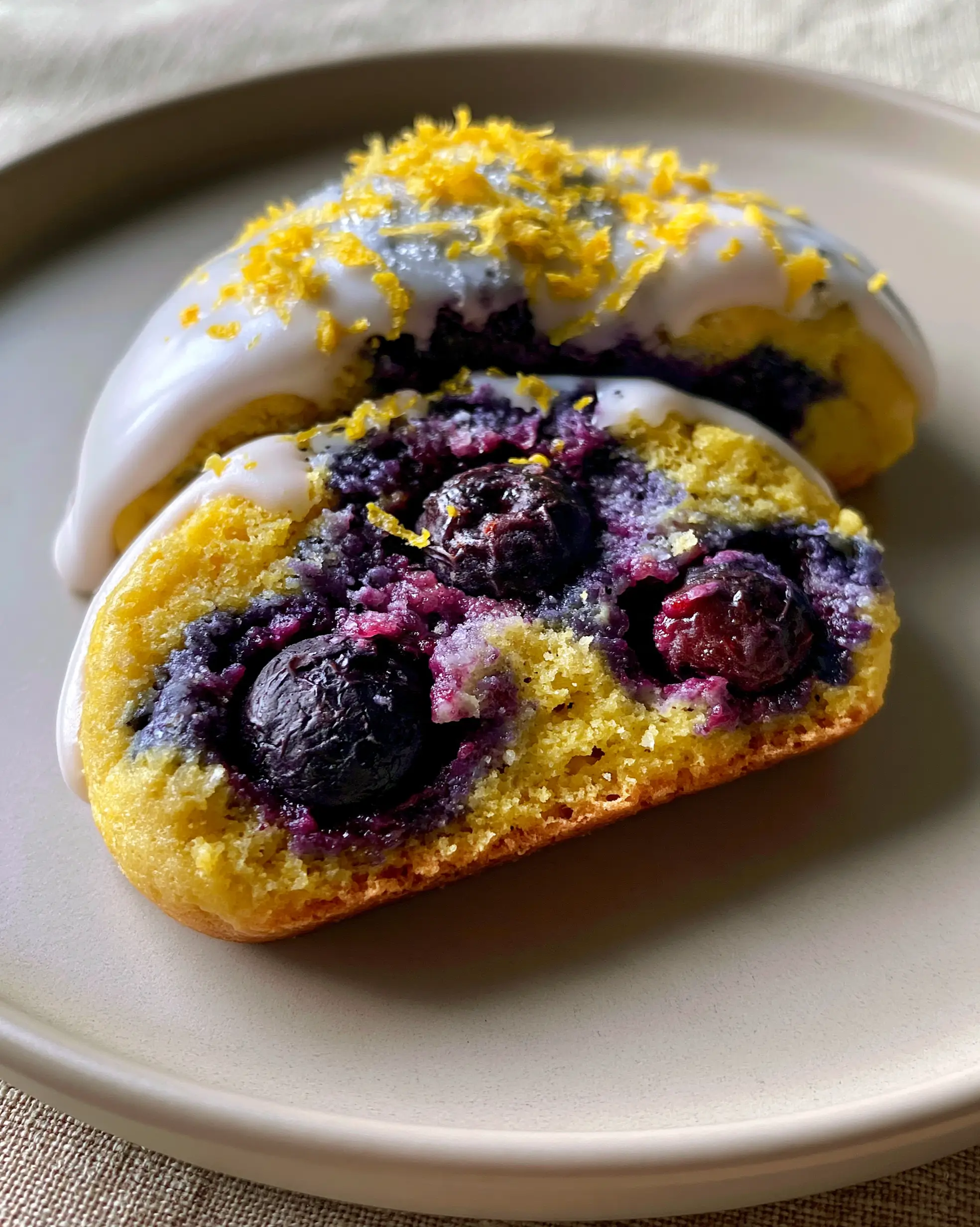 A handheld smartphone photo of a lemon blueberry cookie broken in half to show the soft golden dough and jammy blueberries. (lemon blueberry cookies)