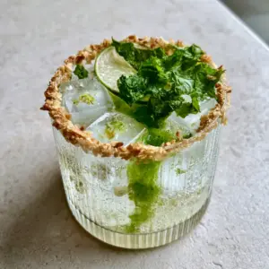 Close up of a Coconut Spritz featuring large square ice cubes and lime zest.
