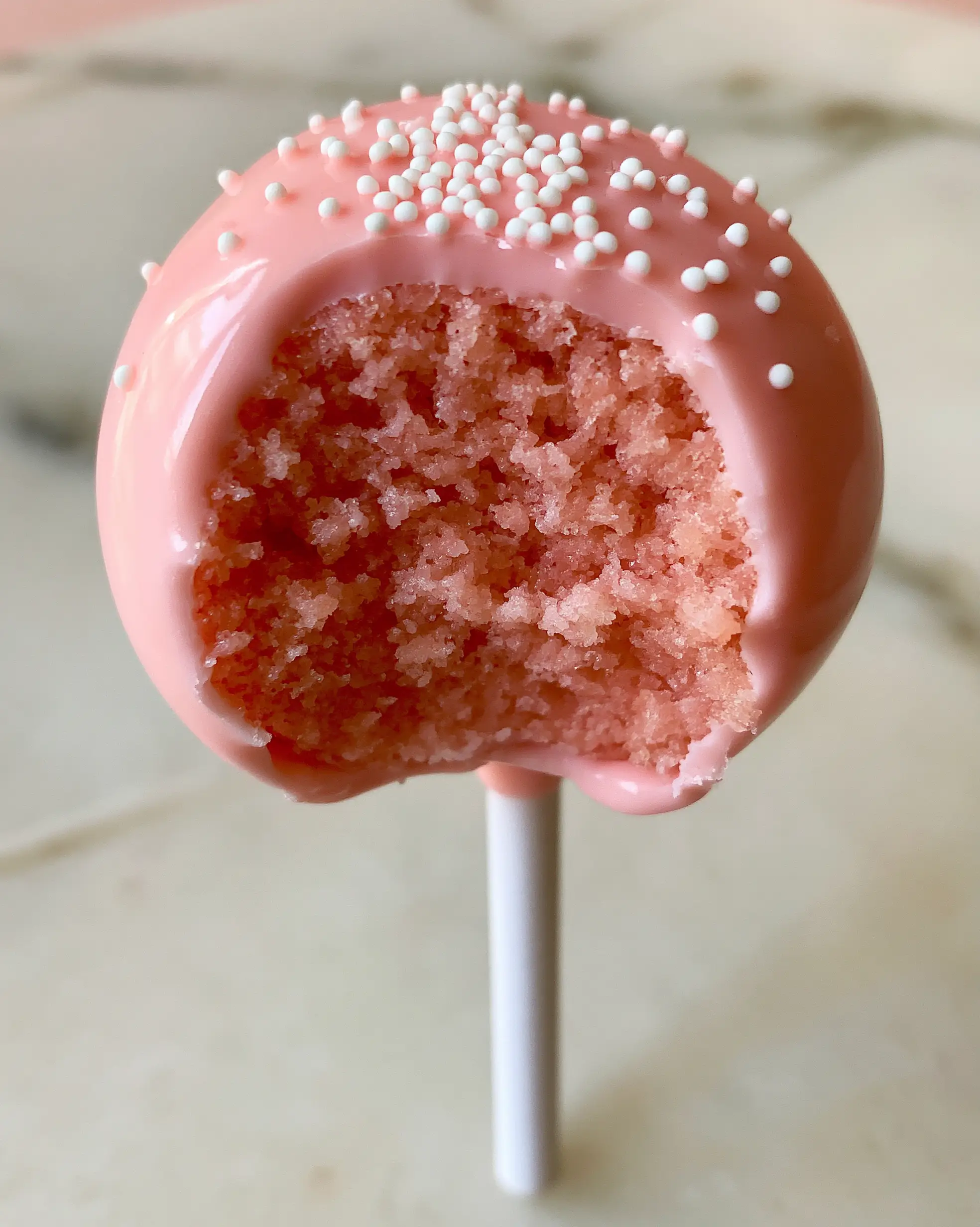 A close-up view of a pink cake pop revealing the dense moist pastel pink interior. (cake pop flavors)