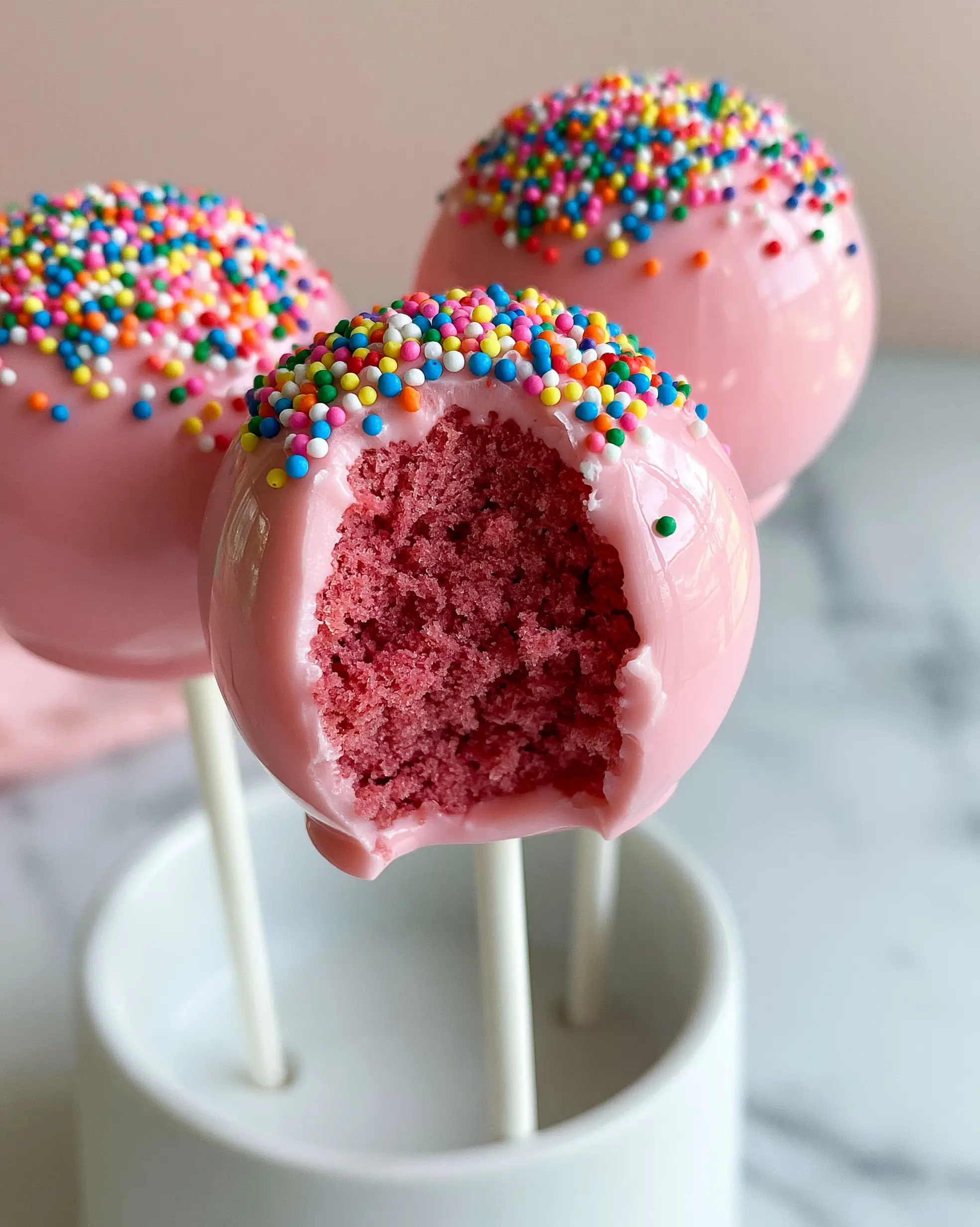 A close-up of a Birthday Cake Pop with a clean bite taken out, revealing a moist, dense, vibrant pink cake center.
