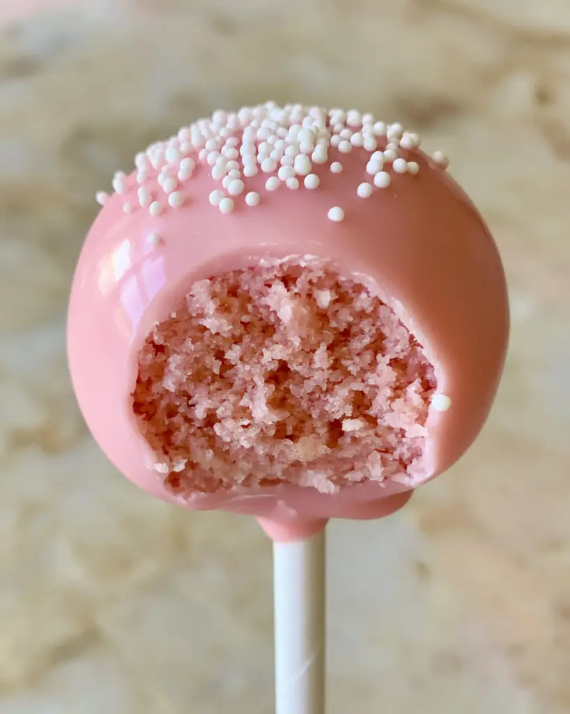 Two pink cake pops held against a bright beige marble background.