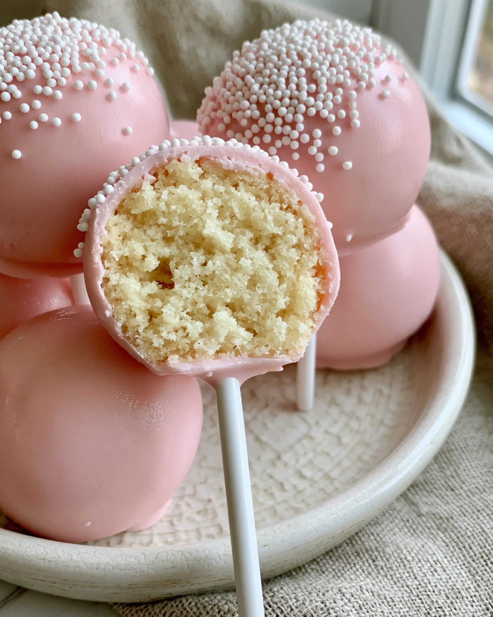 Close-up of a pink cake pop with a clean bite revealing a dense pale-yellow vanilla crumb. (cake pop recipes)
