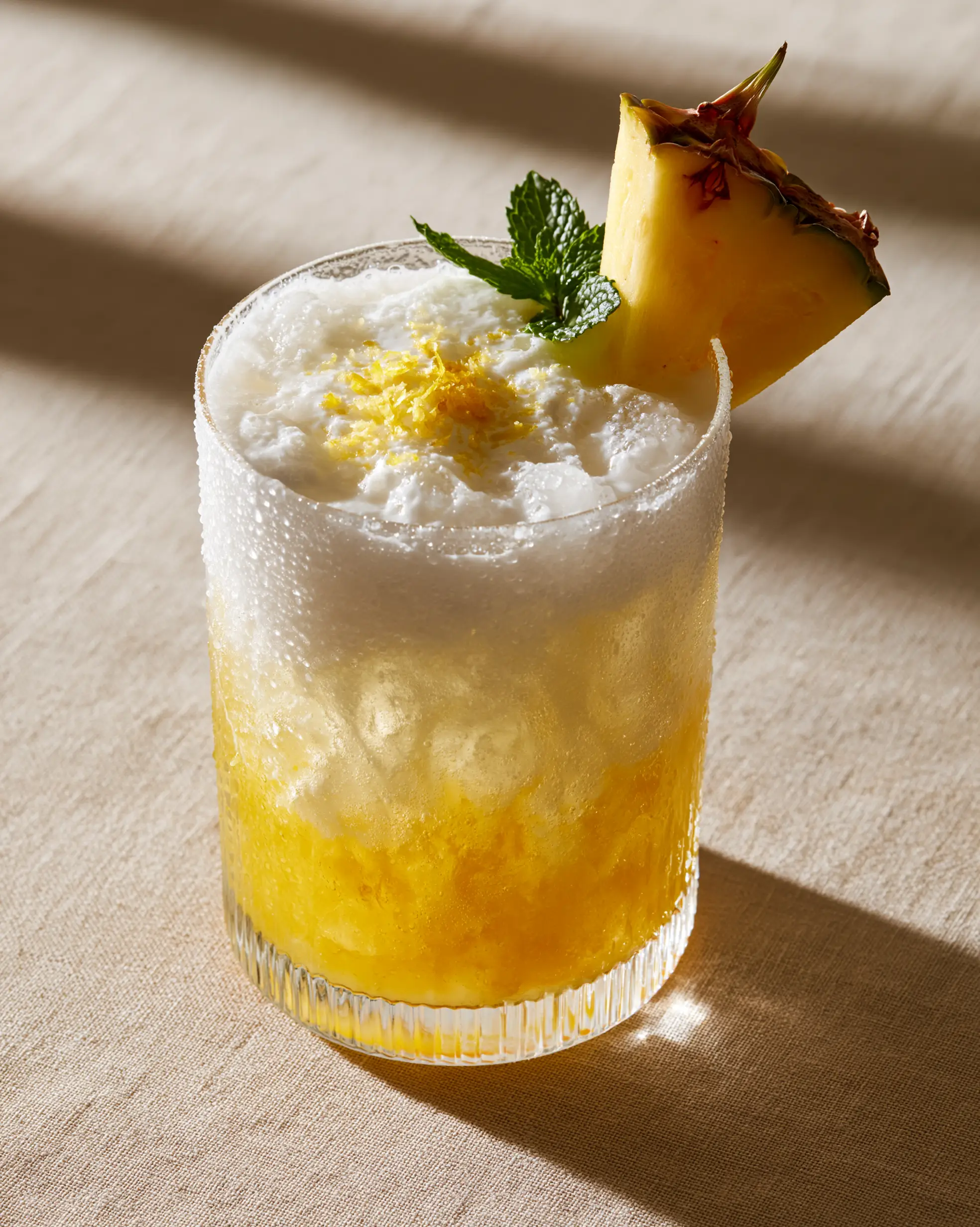 Handheld photo of a coconut pineapple lemonade in morning sunlight showing condensation and crushed ice.