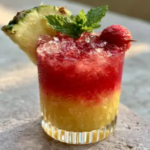 Handheld photo of a Watermelon pineapple chill mocktail showing the ruby and golden layers and condensation.