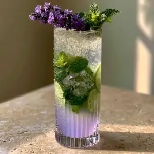 Close up of Lavender Mojito Mocktail showing effervescent bubbles and lime wheels in a ribbed glass.